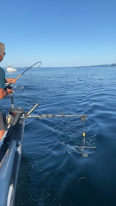 The owner fishing from the side of his boat, using a fishing rod and a CruciFish device.